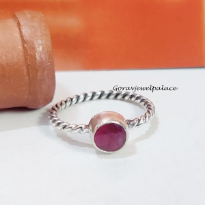 May include: A silver ring with a twisted band and a round, red gemstone.
