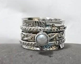 Könnte beinhalten: Ein silberner Drehring mit einem weißen Perlenakzent. Der Ring hat ein florales Design und besteht aus mehreren Bändern.