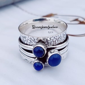 May include: A silver ring with three blue lapis lazuli stones. The ring is made of multiple bands and has a floral design.