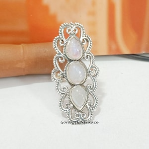 Könnte beinhalten: Ein silberner Ring mit drei birnenförmigen Mondstein-Edelsteinen, die in einem filigranen Design gefasst sind.