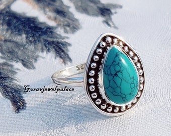 May include: A silver ring with a turquoise teardrop-shaped stone set in a beaded bezel. The ring is on a white background.