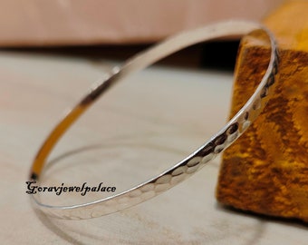 May include: A silver hammered bangle bracelet. The bracelet is simple and elegant, with a smooth, polished finish.