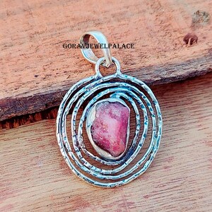 May include: A silver pendant with a pink gemstone set in a circular design of concentric circles.
