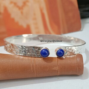 Pode incluir: Pulseira de bracelete de prata com acabamento martelado e dois acentos de pedras preciosas azuis. Goravjewelpalace está impresso na pulseira.