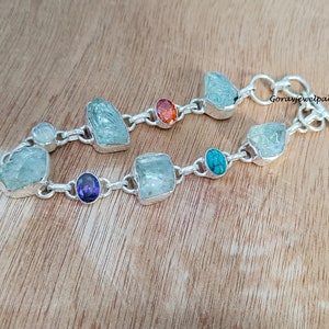 May include: A silver bracelet with a chain and various gemstones, including aquamarine, amethyst, turquoise, and orange. The bracelet has a toggle clasp.