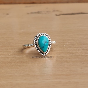 Op de afbeelding: Een zilveren ring met een turquoise traanvormige steen gezet in een gedraaide zilveren band.