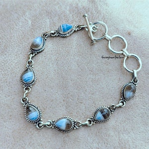 Pode incluir: Um bracelete de prata com fecho de correr apresenta uma fila de pedras em forma de lágrima com padrões azuis e brancos. As pedras são engastadas em prata.