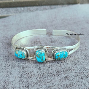 May include: Silver cuff bracelet with three turquoise stones set in silver. The stones are rectangular and have a mottled blue and gold pattern.
