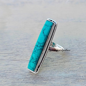 May include: A silver ring with a turquoise stone set in a rectangular shape. The stone has a marbled pattern and is a vibrant blue-green color.