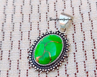 Puede incluir: Un colgante de plata con una piedra turquesa verde engastada en un engaste de plata. El colgante tiene un borde decorativo de pequeñas cuentas de plata.
