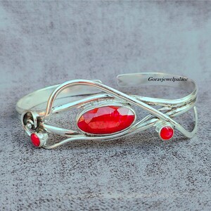 Puede incluir: Una pulsera de plata con una piedra preciosa roja y dos piedras rojas más pequeñas. La pulsera tiene un diseño delicado e intrincado.