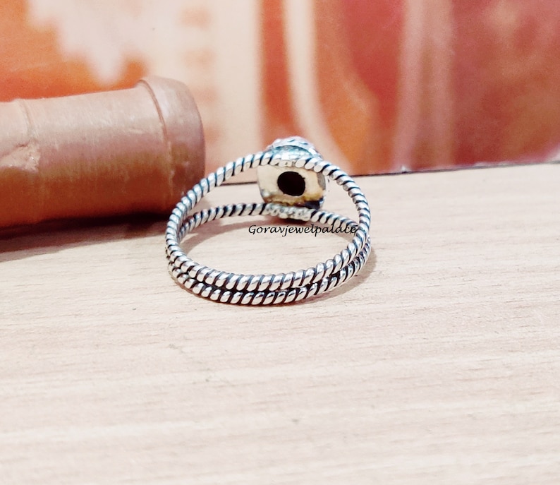 May include: Silver ring with a twisted band and a black gemstone. The ring is on a wooden surface.