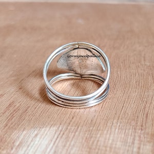 May include: A silver ring with a layered band design. The ring features a central, oval-shaped stone with a textured surface. The ring is set against a wooden background. The text "Goravjewelpalace" is visible on the ring.