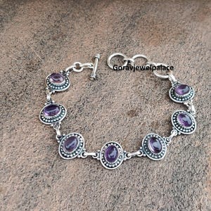Peut inclure: Bracelet en argent orn&eacute; de pierres d'am&eacute;thyste ovales. Chaque am&eacute;thyste est sertie dans une bordure perl&eacute;e. Le bracelet est dot&eacute; d'un fermoir &agrave; bascule. Le texte "Goravjewelpalace" est visible.
