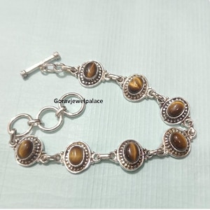 Peut inclure: Bracelet en argent orn&eacute; de pierres d'oeil de tigre ovales. Le bracelet est dot&eacute; d'un fermoir &agrave; bascule et est reli&eacute; par de petits anneaux en argent. Les pierres d'oeil de tigre sont de couleur marron chaud et sont serties dans une lunette en argent.