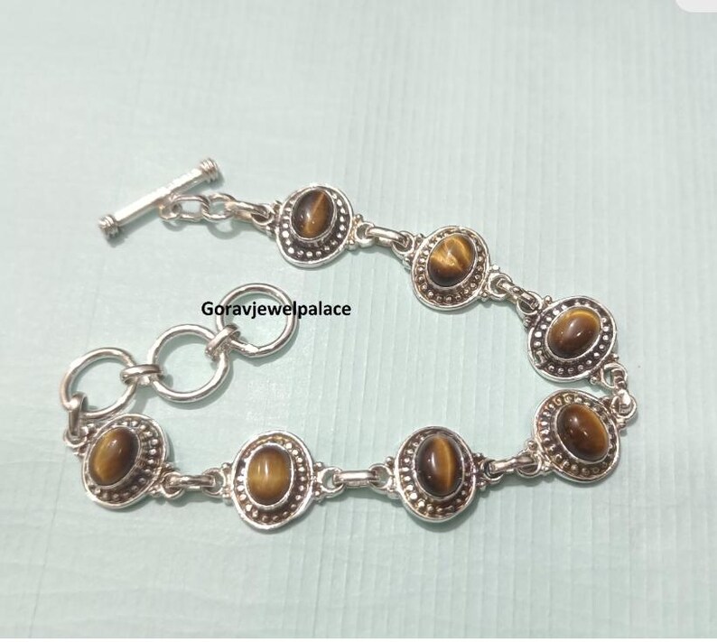 Peut inclure: Bracelet en argent orn&eacute; de pierres d'oeil de tigre ovales. Le bracelet est dot&eacute; d'un fermoir &agrave; bascule et est reli&eacute; par de petits anneaux en argent. Les pierres d'oeil de tigre sont de couleur marron chaud et sont serties dans une lunette en argent.