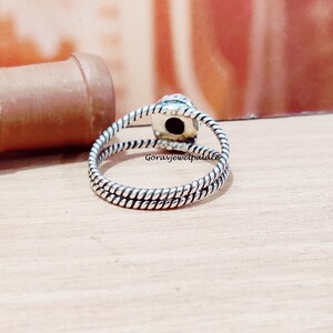 May include: Silver ring with a twisted band and a black gemstone. The ring is on a wooden surface.