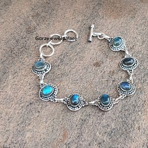 Peut inclure: Bracelet en argent orn&eacute; de pierres ovales de labradorite. Chaque pierre est sertie dans une lunette perl&eacute;e et reli&eacute;e par des maillons en argent. Le bracelet a un fermoir &agrave; bascule et le texte "Goravjewelpalace".
