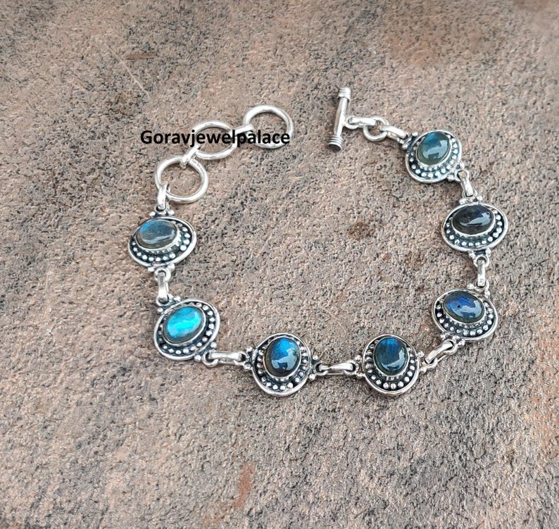 Peut inclure: Bracelet en argent orn&eacute; de pierres ovales de labradorite. Chaque pierre est sertie dans une lunette perl&eacute;e et reli&eacute;e par des maillons en argent. Le bracelet a un fermoir &agrave; bascule et le texte "Goravjewelpalace".