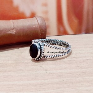 May include: A silver ring with a black oval gemstone set in a twisted band.