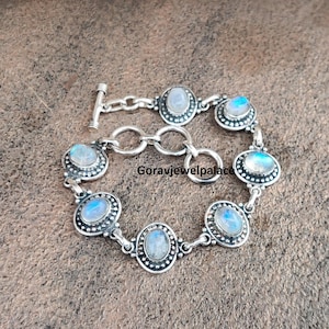 Peut inclure: Un bracelet en argent orn&eacute; de cabochons de pierres de lune ovales et ronds. Le bracelet est dot&eacute; d'un fermoir &agrave; bascule et est compos&eacute; de maillons interconnect&eacute;s. Les pierres de lune ont une lueur iris&eacute;e bleue et blanche.