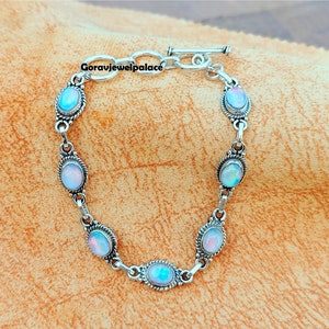 Op de afbeelding: Een zilveren armband met een schuifgesp en zes ovale, iriserende witte stenen.