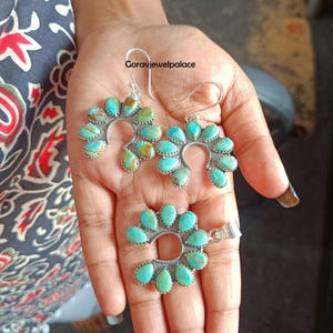 May include: A set of jewellery featuring two earrings and one pendant, each designed in a horseshoe shape with multiple teardrop-shaped turquoise stones set in silver. The text "goravjewelpalace" is visible above the earrings in the centre.