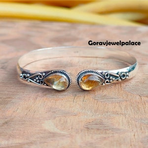 Op de afbeelding: Zilveren armband met twee traanvormige topaas edelstenen. De armband heeft een delicaat bloemmotief.