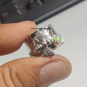 Peut inclure: Bague en argent avec un motif en nid d'abeille et un charme d'abeille. La bague est ornée d'une opale verte.