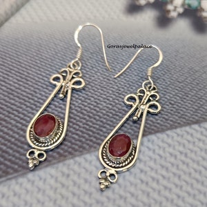 May include: A pair of silver dangle earrings with red gemstone accents. The earrings feature a delicate, ornate design with a teardrop-shaped pendant.