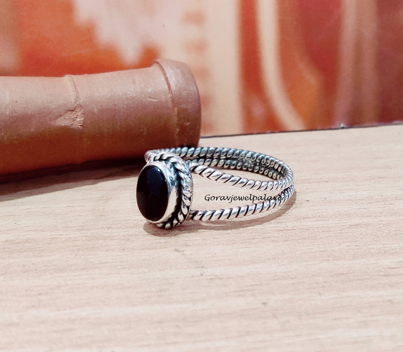 May include: A silver ring with a black oval gemstone set in a twisted band.
