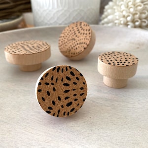 May include: Four wooden knobs with a black and brown abstract pattern. The knobs are round and have a flat top.
