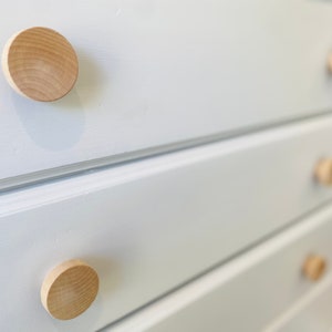 May include: White chest of drawers with four drawers and wooden knobs. The dresser has a simple design and is made of wood.