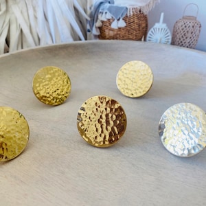 May include: Four round, hammered metal decorative pieces. Three are gold and one is silver. They are arranged on a light wood surface.