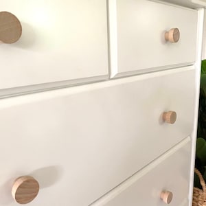 May include: White dresser with six drawers and wooden knobs. The dresser has a simple design and is made of wood.