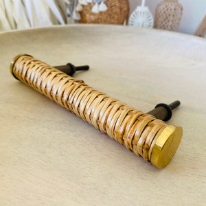 May include: A woven rattan cabinet pull with brass end caps. The pull is light brown and has a natural woven texture.