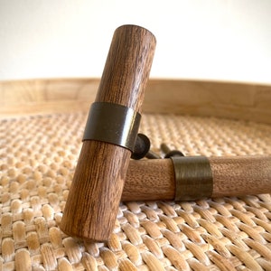 Może przedstawiać: Dwa drewniane gałki do szafek z mosiężną listwą ozdobną. Gałki są brązowe i mają wzór słojów drewna.