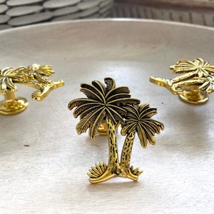 May include: Three gold palm tree drawer pulls. The palm trees are detailed and have a textured finish.