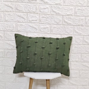 May include: A dark green rectangular pillow with a textured surface and small round bumps. The pillow is sitting on a white stool.