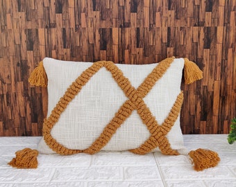 May include: White throw pillow with a geometric pattern of brown woven tassels. The pillow has a rectangular shape and is accented with tassels on each corner.