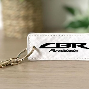 May include: White leather keyring with a black CBR Fireblade logo. The keyring has a gold metal ring and a gold metal clip.
