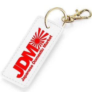 Op de afbeelding: Witte sleutelhanger met een rood "JDM" logo en de tekst "Japanese Domestic Market". Het logo heeft een rode opkomende zon.