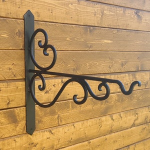 May include: Black metal wall-mounted bracket with decorative scrollwork. The bracket is designed to hold a sign or other object.