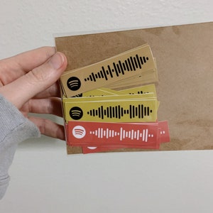 May include: A stack of yellow and red rectangular stickers with a black Spotify logo and a black barcode. The stickers are on a brown background.