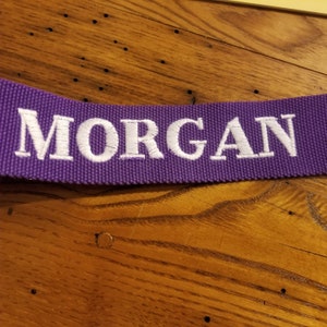 May include: Purple fabric strap with the name "MORGAN" embroidered in white.