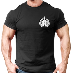 Może przedstawiać: Czarny t-shirt z białym nadrukiem przedstawiającym hełm spartański z wieńcem laurowym.