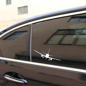 May include: A white airplane silhouette decal on a black car window.