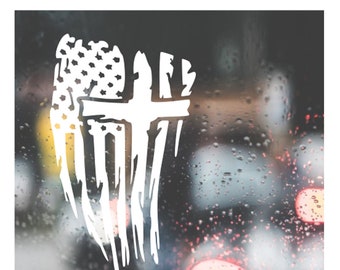 May include: A white distressed American flag with a cross superimposed over it. The flag is on a blurry background of raindrops on a window.