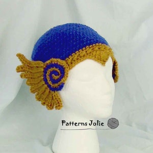 Könnte beinhalten: Eine blaue und goldene Häkelmütze mit einem Spiralmuster an der Seite. Die Mütze sitzt auf einem weißen Mannequin-Kopf. Der Text "Patterns Jolie" ist unter der Mütze sichtbar.