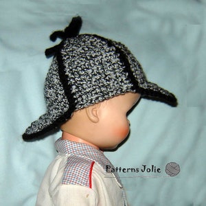 Può includere: Un cappello a uncinetto nero e grigio con una visiera e una cima a punta. Il cappello ha un bordo nero attorno alla visiera e alla cima. Il cappello è indossato da un bambino.